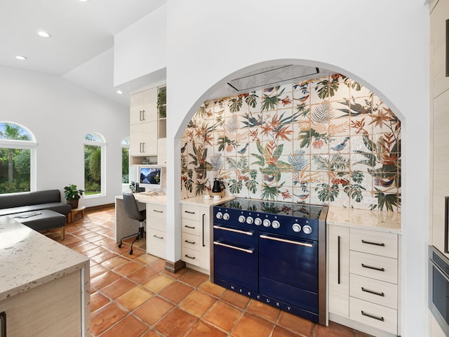 kitchen featuring light tile patterned flooring, high vaulted ceiling, electric range, light stone counters, and white cabinetry