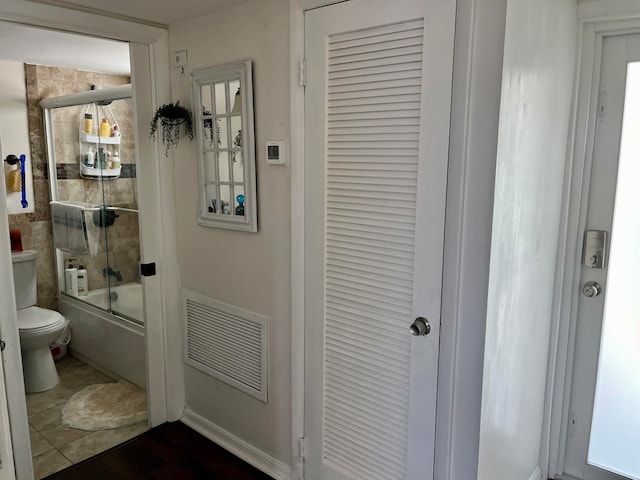 bathroom with tile patterned floors, toilet, and bath / shower combo with glass door