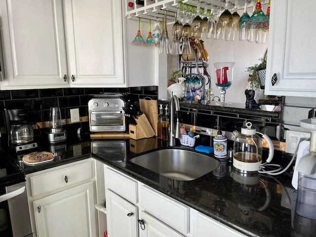 kitchen featuring white cabinets, dark stone counters, sink, and backsplash