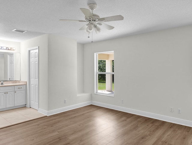 interior space featuring light wood-type flooring, a textured ceiling, connected bathroom, and ceiling fan