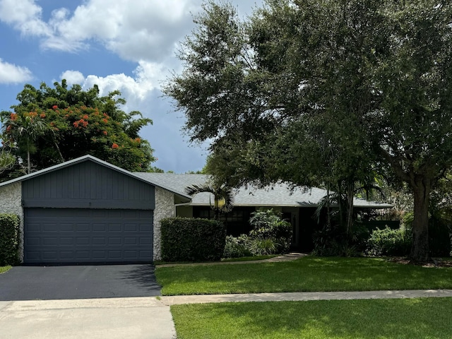 view of front of home featuring a garage, a front yard, stone siding, and aphalt driveway