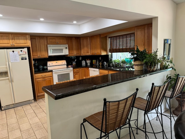 kitchen with kitchen peninsula, white appliances, backsplash, dark stone countertops, and a kitchen bar