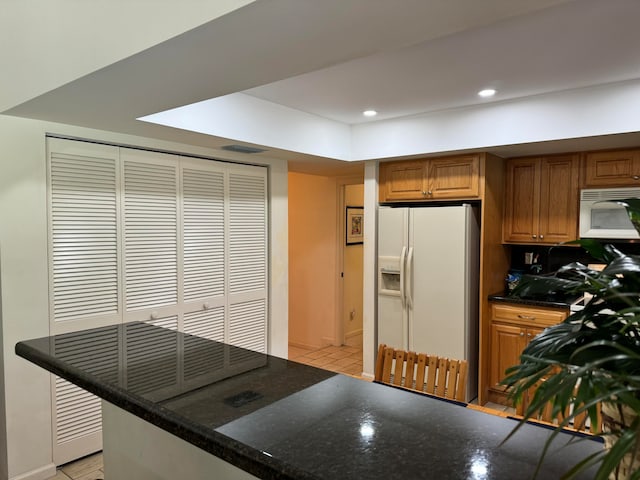 kitchen featuring white appliances, light tile patterned floors, kitchen peninsula, and dark stone counters