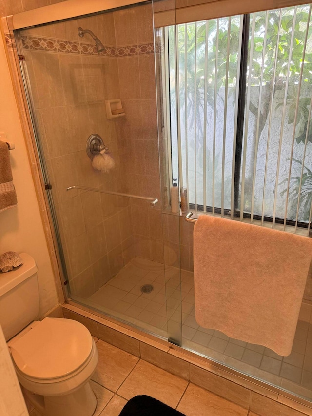 bathroom featuring a shower with shower door, toilet, and tile patterned flooring