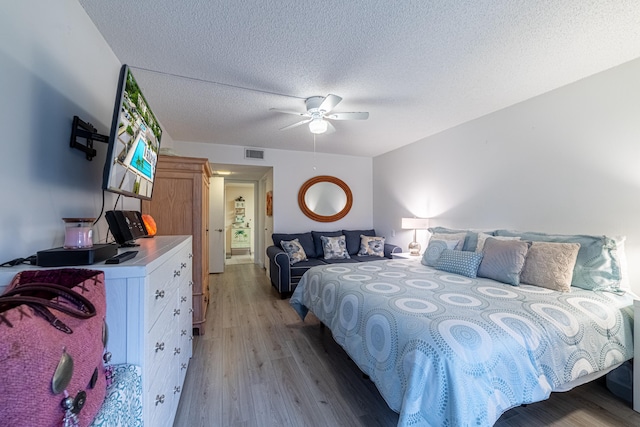 bedroom with light wood-type flooring, ceiling fan, and a textured ceiling