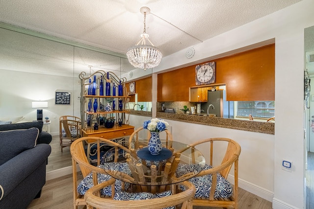 dining area with sink, an inviting chandelier, light hardwood / wood-style floors, and a textured ceiling