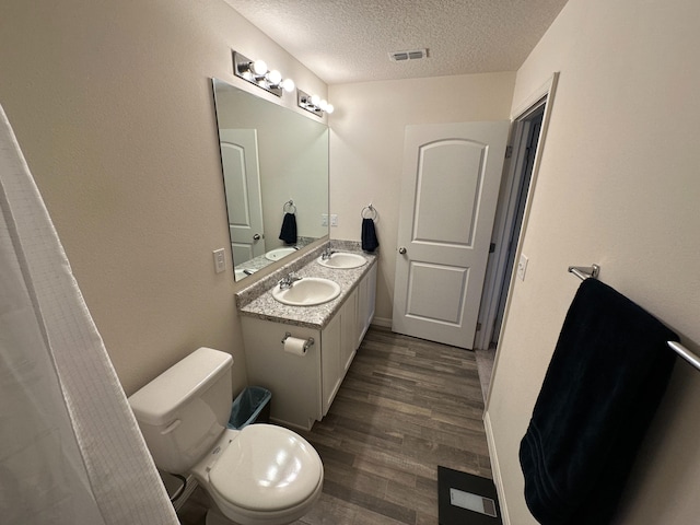 bathroom with toilet, wood-type flooring, vanity, and a textured ceiling