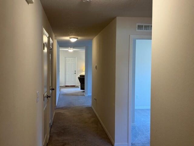 corridor featuring a textured ceiling and light carpet