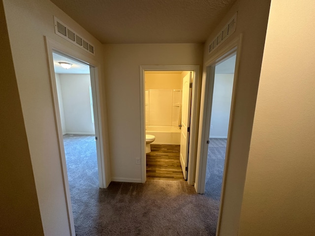 hall with dark carpet and a textured ceiling