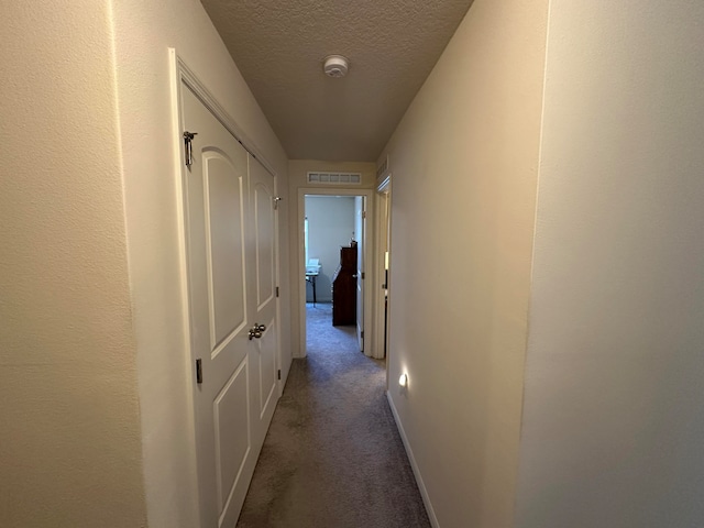 corridor with a textured ceiling and carpet floors