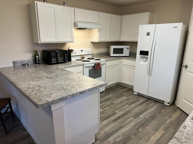 kitchen with white appliances, a breakfast bar, white cabinetry, and dark hardwood / wood-style flooring