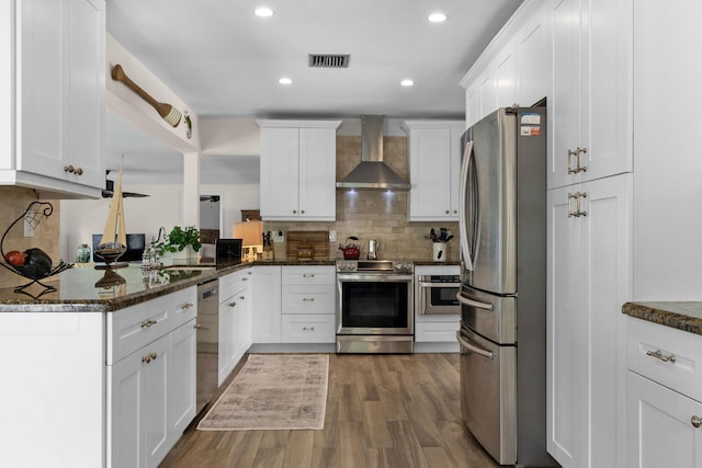 kitchen with white cabinetry, wall chimney range hood, stainless steel appliances, and dark stone counters