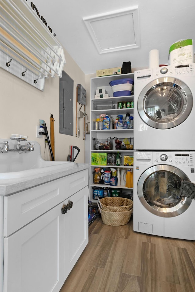 clothes washing area with cabinets, light hardwood / wood-style floors, sink, stacked washer and clothes dryer, and electric panel