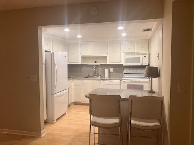 kitchen featuring white appliances, a breakfast bar area, white cabinetry, decorative backsplash, and light hardwood / wood-style flooring