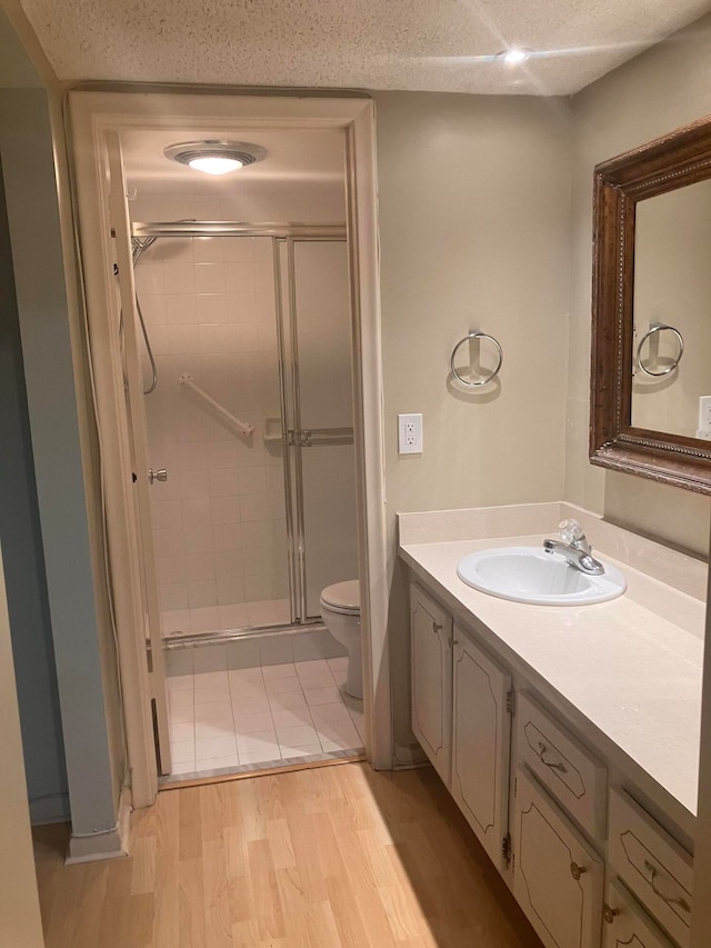 bathroom with wood-type flooring, a textured ceiling, an enclosed shower, toilet, and vanity