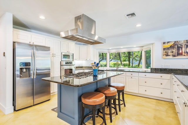 kitchen featuring dark stone counters, a center island, appliances with stainless steel finishes, light tile patterned floors, and island exhaust hood