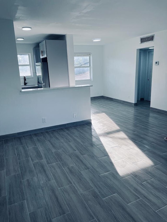 unfurnished living room with wood tiled floor, a healthy amount of sunlight, visible vents, and baseboards