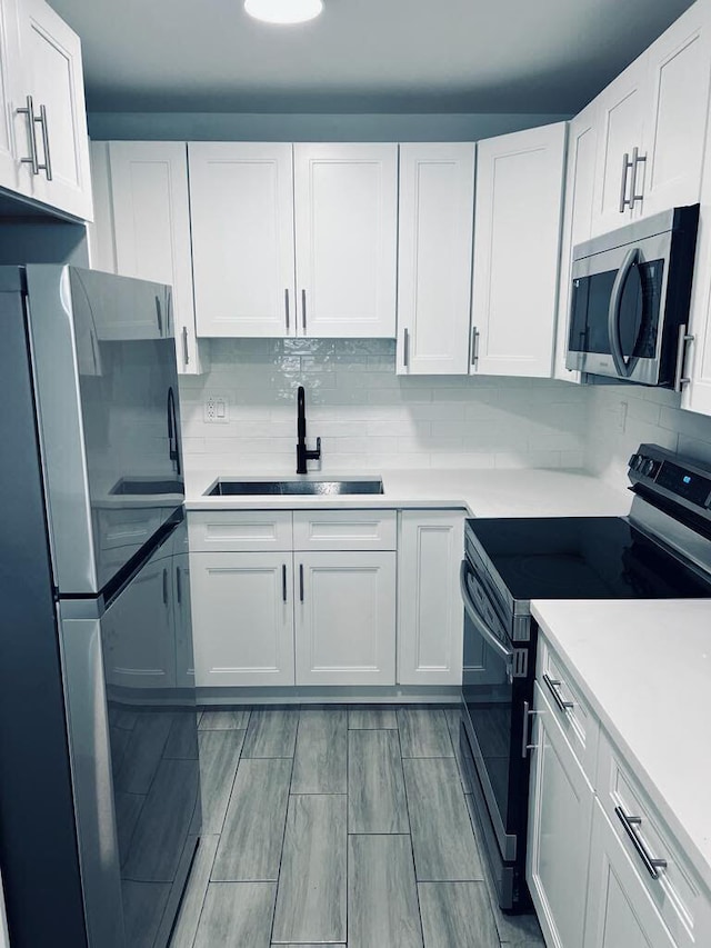 kitchen featuring stainless steel appliances, a sink, white cabinetry, light countertops, and tasteful backsplash