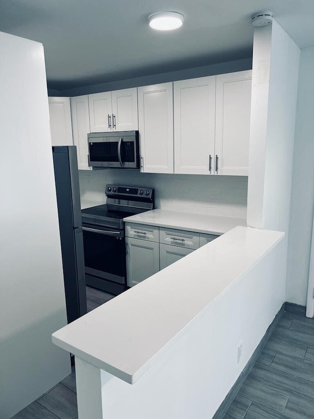 kitchen with a peninsula, white cabinetry, stainless steel appliances, and light countertops