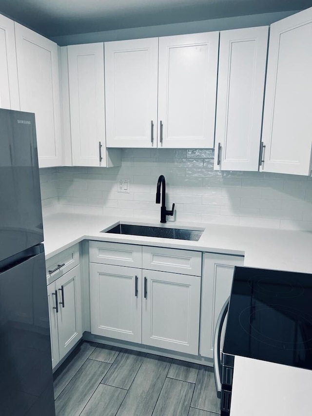 kitchen featuring black appliances, backsplash, a sink, and light countertops