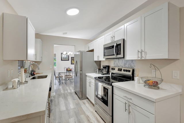 kitchen featuring sink, a notable chandelier, light wood-type flooring, appliances with stainless steel finishes, and white cabinets