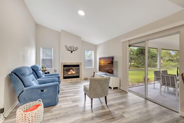 living room with light hardwood / wood-style flooring, vaulted ceiling, and a tiled fireplace