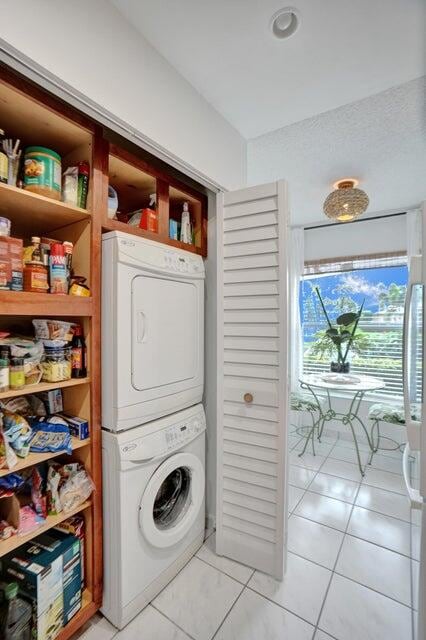 clothes washing area with stacked washer / drying machine and light tile patterned floors