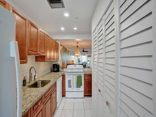 kitchen with sink, light stone counters, white appliances, ceiling fan, and hanging light fixtures