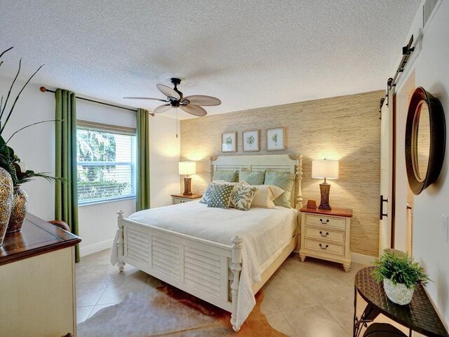 tiled bedroom with ceiling fan, a textured ceiling, and a barn door