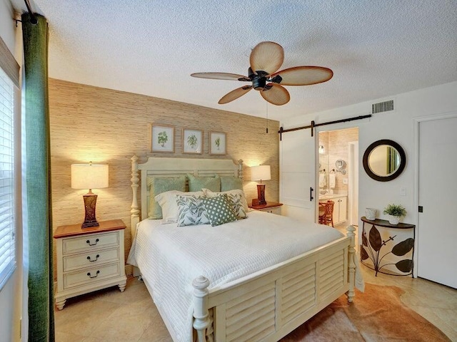 tiled bedroom featuring a textured ceiling, ceiling fan, ensuite bathroom, and a barn door