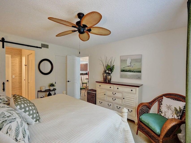 bedroom with a textured ceiling, ceiling fan, and a barn door