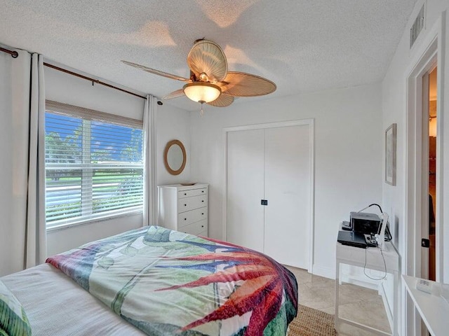 tiled bedroom featuring ceiling fan, a textured ceiling, and a closet