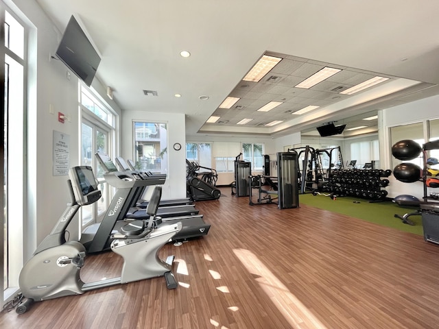 workout area with visible vents, a raised ceiling, and wood finished floors