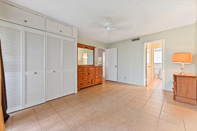 unfurnished bedroom featuring light tile patterned floors, a closet, ceiling fan, and ensuite bathroom