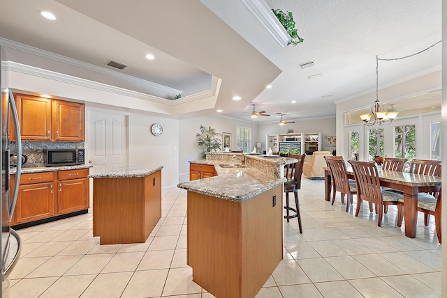 kitchen featuring ceiling fan with notable chandelier, a center island, ornamental molding, and stainless steel appliances