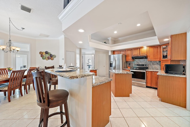 kitchen with stainless steel appliances, decorative light fixtures, ornamental molding, a center island with sink, and light stone countertops