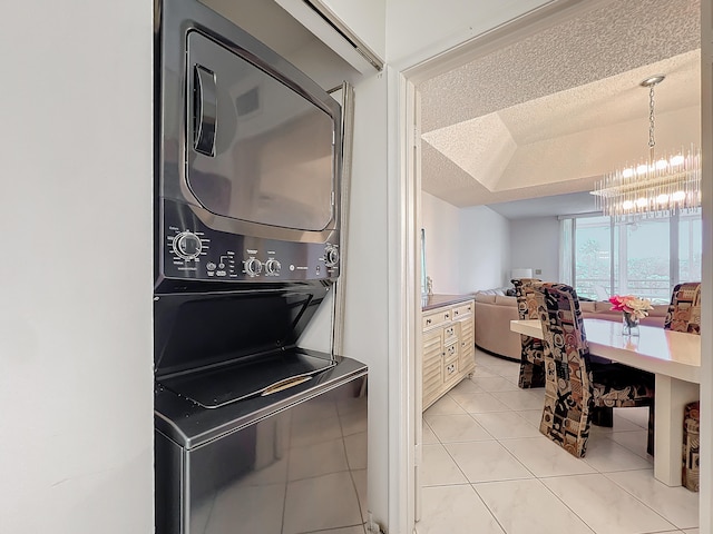 clothes washing area with a textured ceiling, a notable chandelier, light tile patterned flooring, and stacked washer / dryer