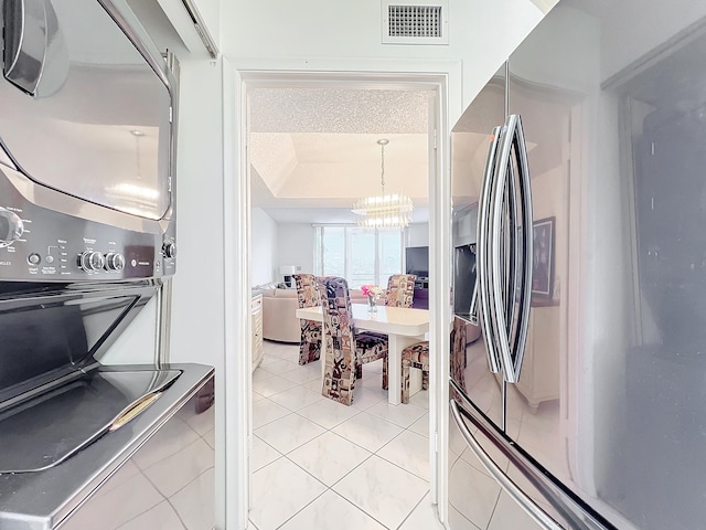 kitchen with stainless steel refrigerator with ice dispenser, a tray ceiling, light tile patterned floors, a notable chandelier, and a textured ceiling