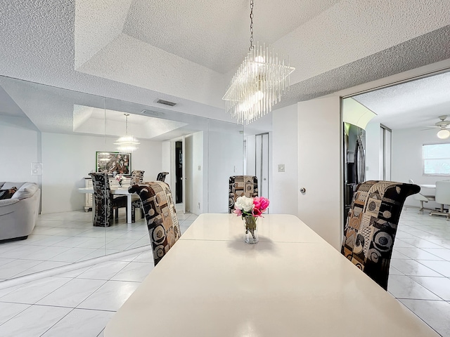 tiled dining area with ceiling fan with notable chandelier, a textured ceiling, and a tray ceiling