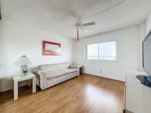 living area with a ceiling fan, light wood-type flooring, and a textured ceiling