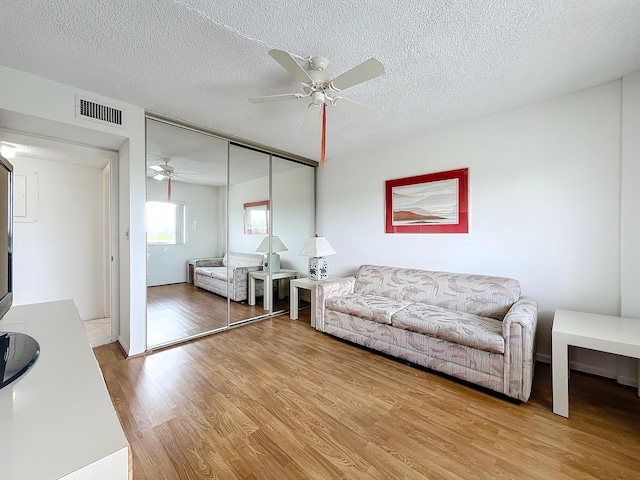 living area with visible vents, ceiling fan, a textured ceiling, and wood finished floors