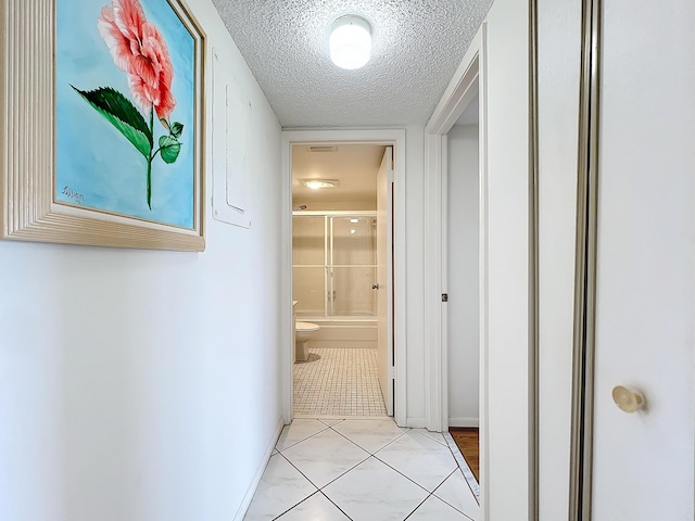 hall with a textured ceiling, baseboards, and light tile patterned floors