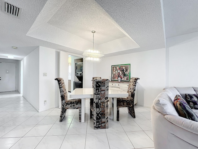 tiled dining space with a textured ceiling, a notable chandelier, visible vents, baseboards, and a tray ceiling