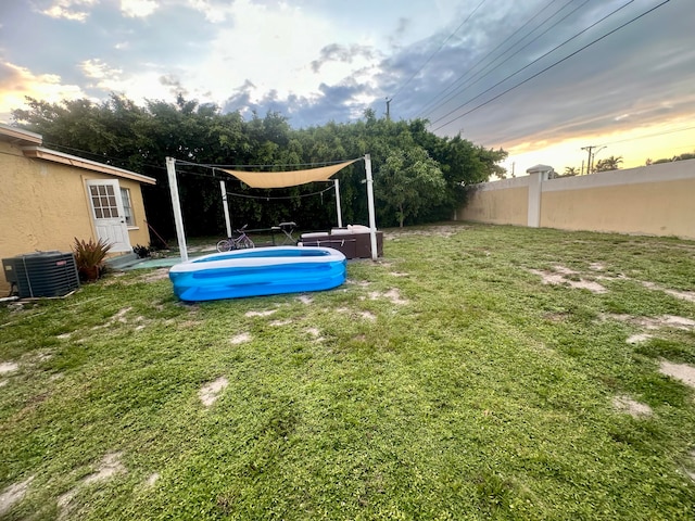 yard at dusk featuring central AC unit and a fenced in pool