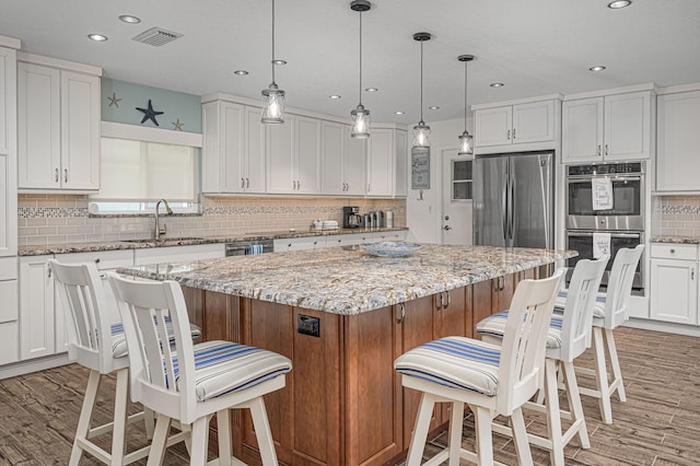 kitchen with appliances with stainless steel finishes, wood-type flooring, a center island, and light stone countertops