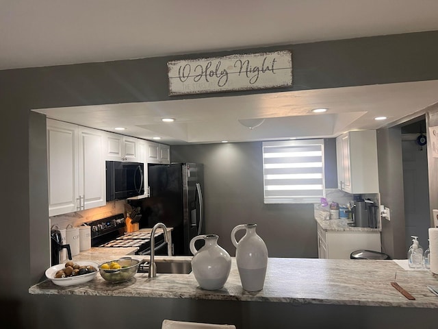 kitchen with a raised ceiling, backsplash, white cabinets, gas stove, and sink