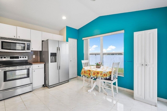 kitchen with stainless steel appliances, lofted ceiling, white cabinets, and light tile patterned floors