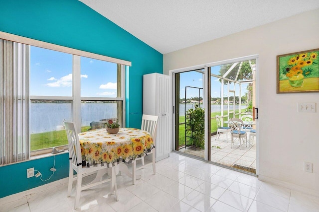 dining space featuring light tile patterned floors, vaulted ceiling, a textured ceiling, and a water view