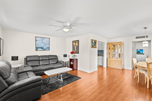 living room featuring light wood-style flooring, visible vents, ceiling fan, and baseboards