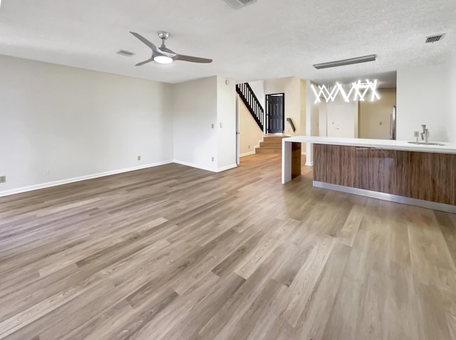 unfurnished living room with hardwood / wood-style flooring, ceiling fan, sink, and a textured ceiling